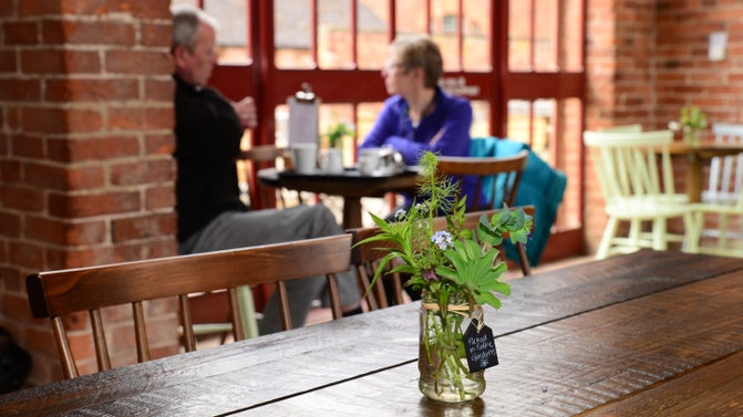 Hand-picked flowers on a table in the restaurant at Calke Abbey, with two visitors enjoying refreshments in the background